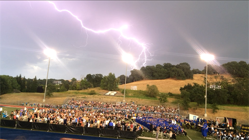 Students gathered outside while lightning strikes in the distance